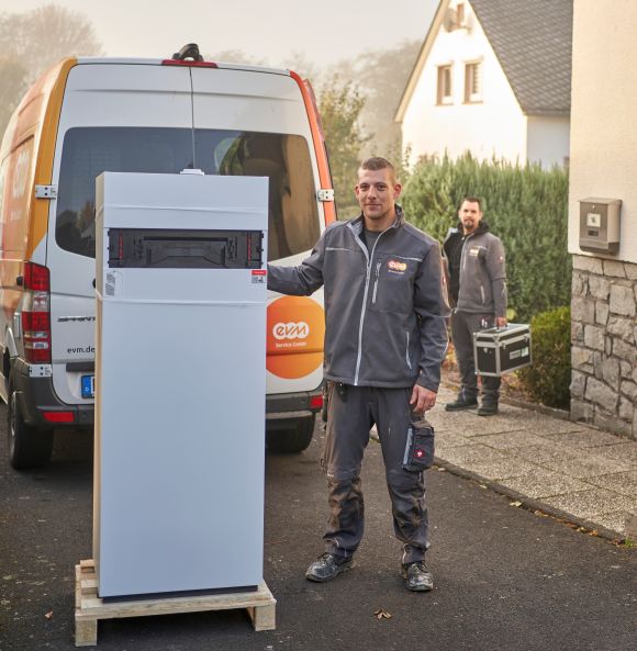 Zwei Männer in evm-Arbeitskleidung stehen vor einem Haus mit einer Heizung