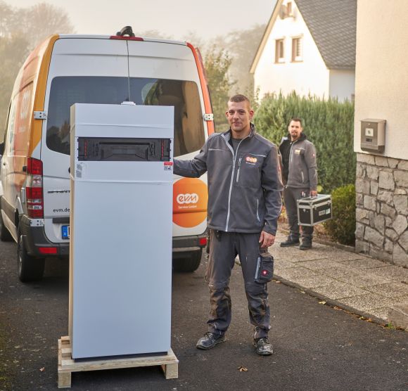 Zwei Männer in evm-Arbeitskleidung stehen vor einem Haus mit einer Heizung