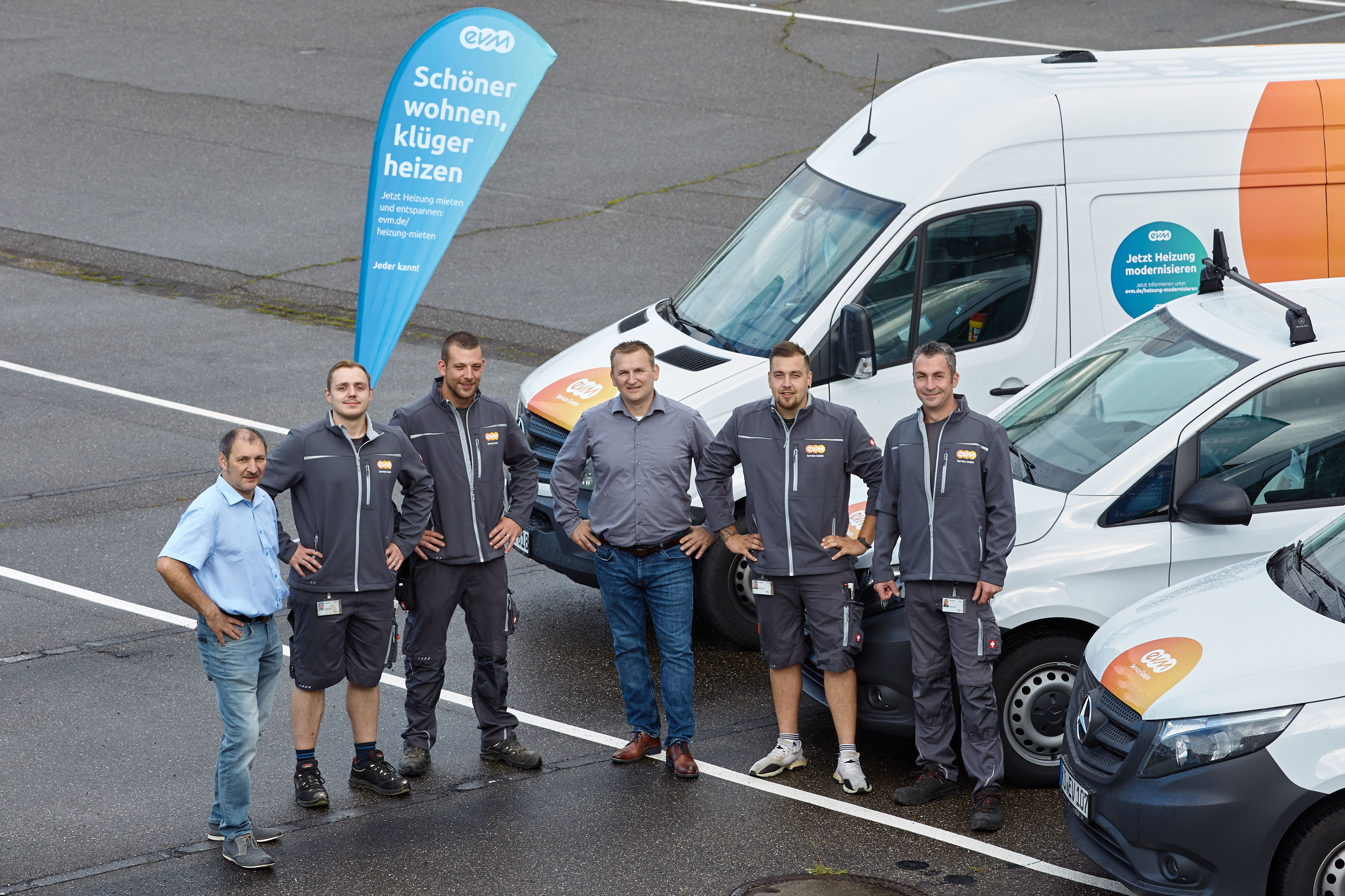Sechs Männer stehen auf einem Parkplatz vor evm-Autos