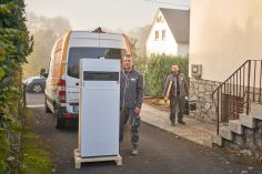 Zwei Männer in evm-Arbeitskleidung stehen vor einem Haus mit einer Heizung